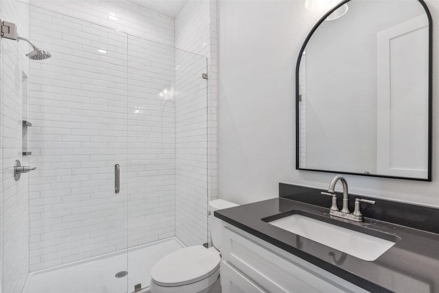 A well-lit guest bathroom features a spacious glass-enclosed shower and a sleek vanity.