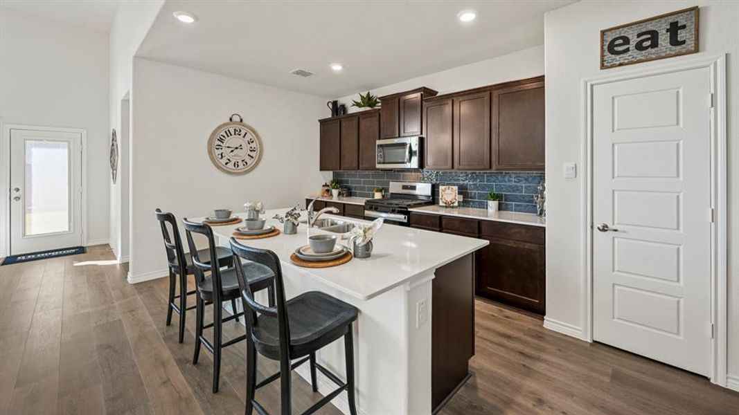 Kitchen featuring an expansive island with seating, white countertops, dark wood-finish cabinetry, stainless steel appliances, and a blue subway tile backsplash Kitchen featuring an expansive island with seating, white countertops, dark wood-finish cabinetry, stainless steel appliances, and a blue subway tile backsplash
