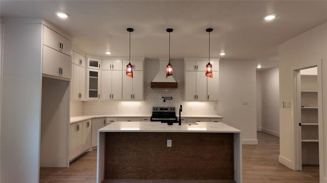 Kitchen featuring white cabinets, an island with sink, wood tiled floors, glass insert cabinets, and tasteful backsplash Kitchen featuring white cabinets, an island with sink, wood tiled floors, glass insert cabinets, and tasteful backsplash