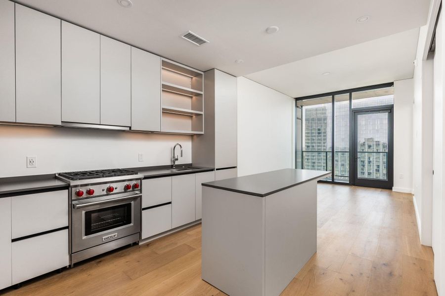 A streamlined modern kitchen flows into an open-concept living area with floor-to-ceiling windows offering urban panoramas.