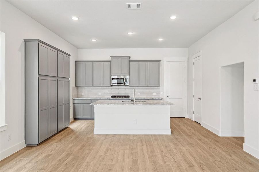 Kitchen with light wood-type flooring, gray cabinets, tasteful backsplash, sink, and a center island with sink