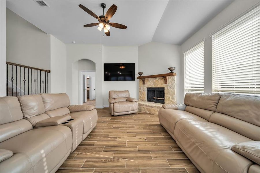Living room with wood finish floors, ceiling fan, a stone fireplace, and arched walkways Living room with wood finish floors, ceiling fan, a stone fireplace, and arched walkways