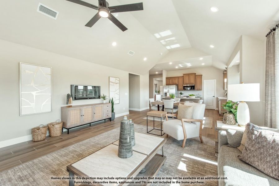 Open-concept living room with vaulted ceiling, ceiling fan, and wood-look floors leading to kitchen and dining area