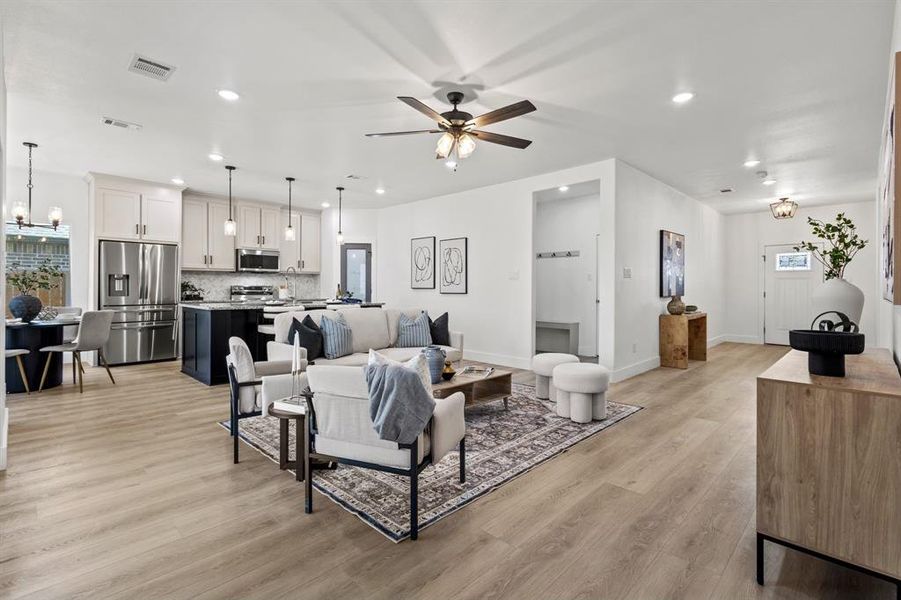 Living area with visible vents, baseboards, light wood-type flooring, recessed lighting, and ceiling fan with notable chandelier