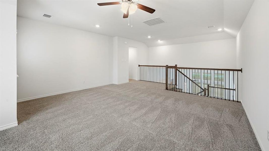Spacious loft featuring plush grey carpeting, a multi-speed ceiling fan, recessed lighting, and a dark wood and iron railing overlooking the lower level