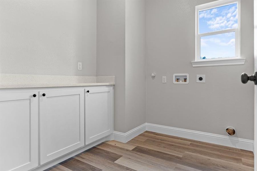 Washroom featuring hookup for an electric dryer, light wood-type flooring, washer hookup, baseboards, and cabinet space Washroom featuring hookup for an electric dryer, light wood-type flooring, washer hookup, baseboards, and cabinet space