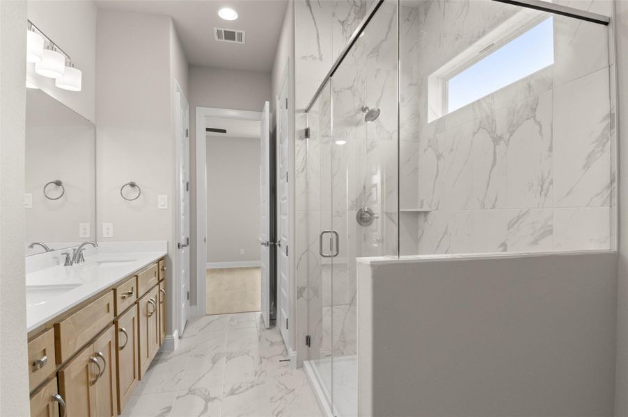 Full bath with marble look tile flooring, a marble finish shower, and double vanity