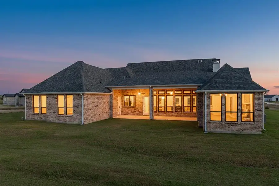 Rear view of property featuring a patio, a yard, a shingled roof, and brick siding