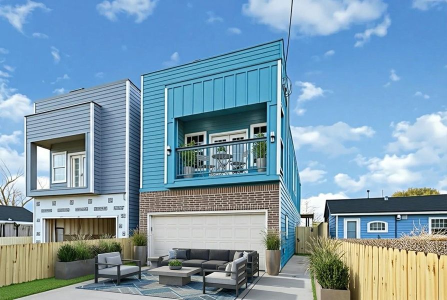 Modern two-story home with vibrant blue siding and a brick-accented ground floor. Features a cozy balcony, a two-car garage, and a fenced yard with outdoor seating. Ideal for those seeking a stylish, contemporary living space.