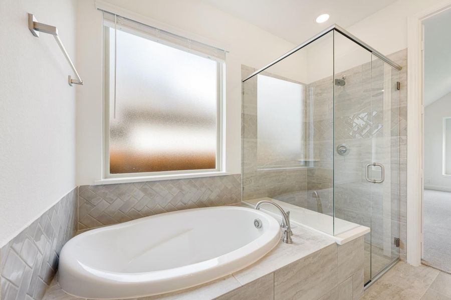 Bathroom with oval soaking tub, glass-enclosed shower, and gray herringbone tile surround Bathroom with oval soaking tub, glass-enclosed shower, and gray herringbone tile surround