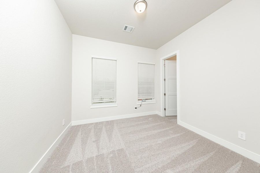 Tucked peacefully in the front of the home is this secondary bedroom. It features a sloped ceiling, plush carpet flooring, large windows with fitted blinds, and a walk-in closet.