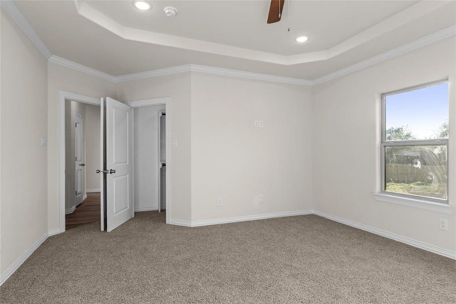 Unfurnished bedroom featuring a tray ceiling, recessed lighting, light colored carpet, ornamental molding, and a ceiling fan