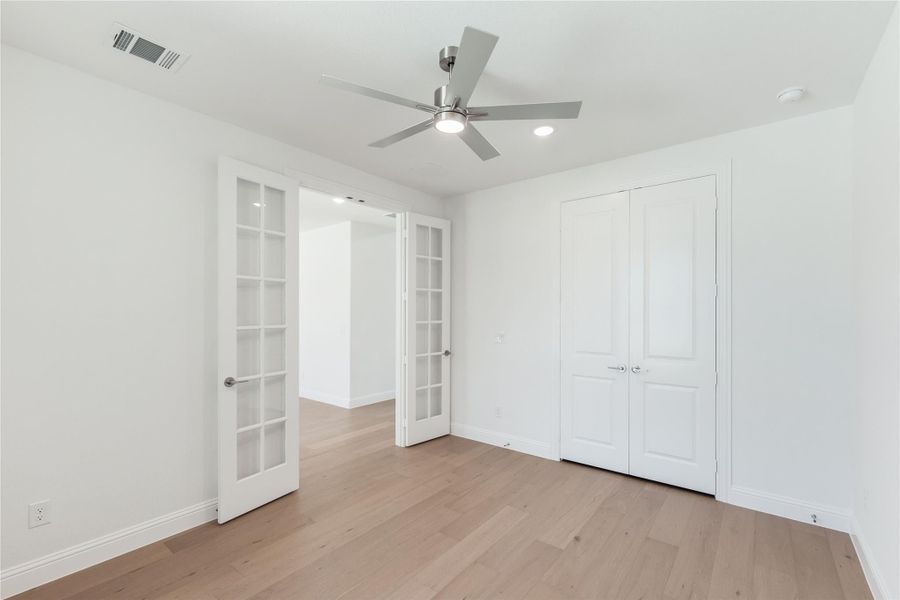 Empty bedroom with French doors, double closet, ceiling fan, and light hardwood floors