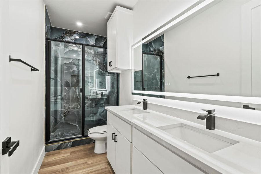 Bathroom with double vanity, a marble finish shower, and light wood-style floors