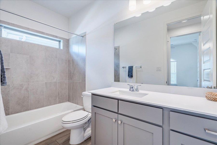 The bathroom features a bathtub with tiled surround, a window, a vanity with a sink, and a toilet