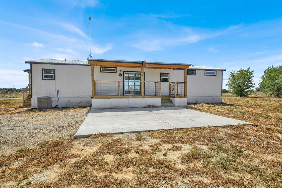 An expansive concrete patio extends from the covered wooden porch of this rural home.