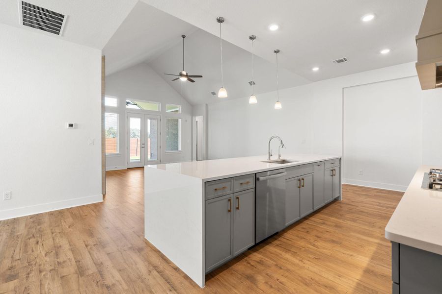 An inviting open-concept kitchen features a spacious island, gleaming countertops, and vaulted ceilings with ample recessed and pendant lighting.