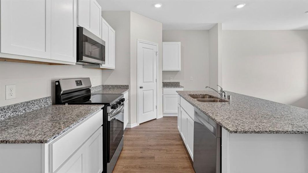 Modern kitchen featuring white cabinetry, speckled countertops, stainless steel appliances, and wood-finish flooring Modern kitchen featuring white cabinetry, speckled countertops, stainless steel appliances, and wood-finish flooring