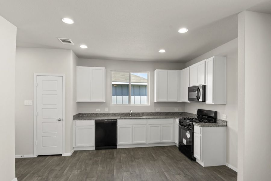 Image of home kitchen with white cabinets and black appliances. Wood-look floors, white walls, and a window over the sink