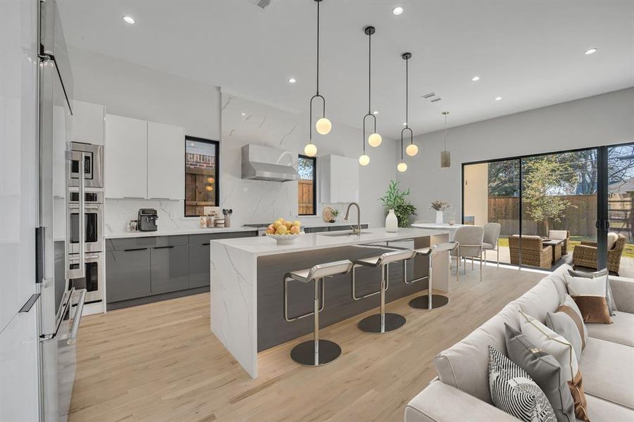 Kitchen with hanging light fixtures, gray cabinets, an island with sink, a kitchen bar, and extractor fan