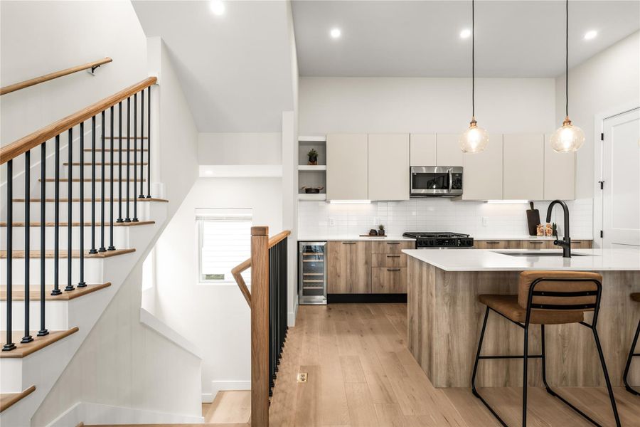 Arriving on the main level reveals the kitchen alongside an open stair design with wood handrails and black metal balusters.