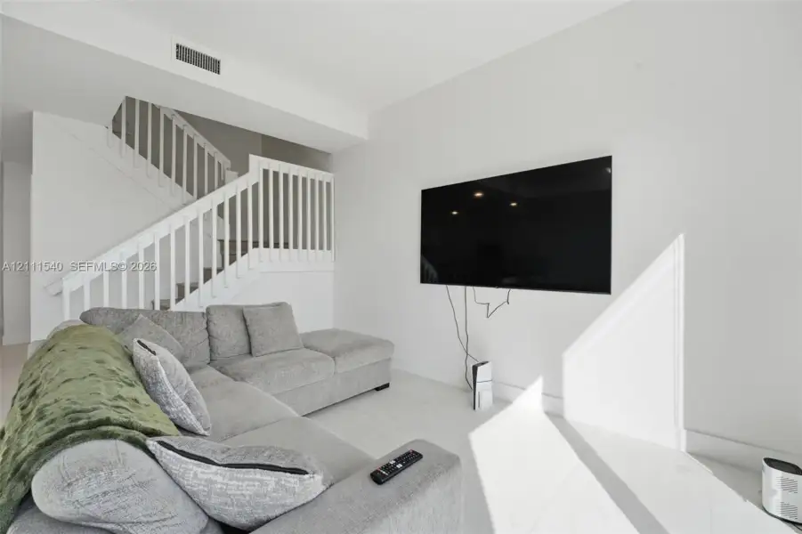 Neutral interior featuring large-format tile flooring, crisp white walls, and a staircase with white vertical balusters
