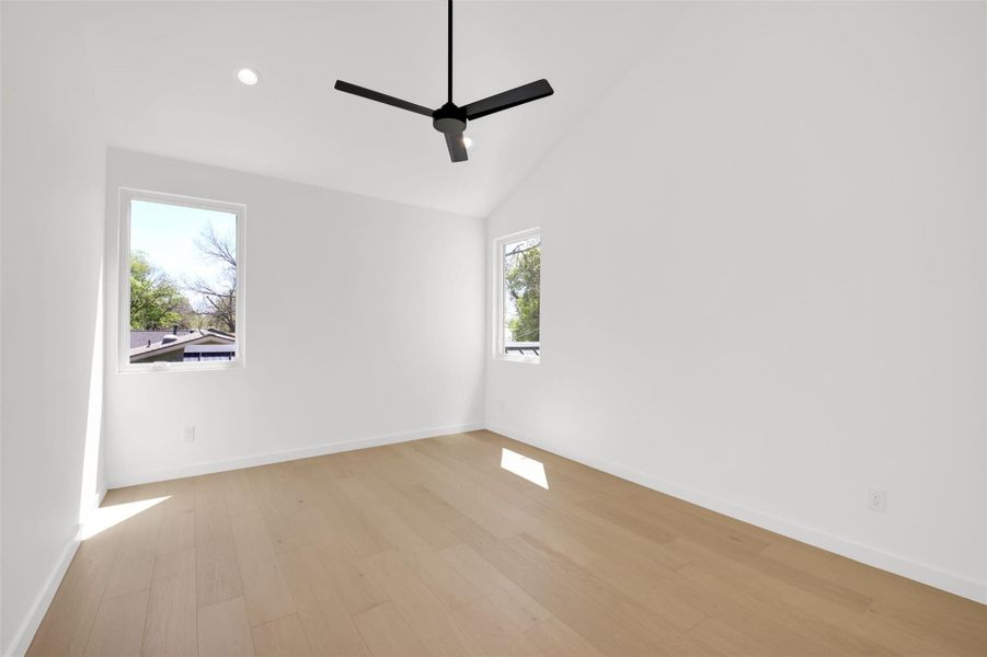 Spare room featuring light wood-style floors, a ceiling fan, lofted ceiling, and recessed lighting with attached bathroom