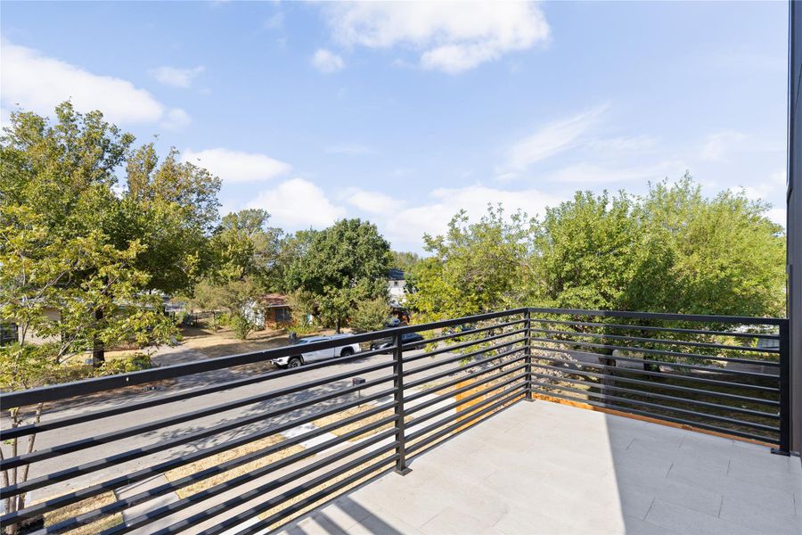 An elevated terrace with sleek metal railings overlooks a tree-lined street under blue skies.