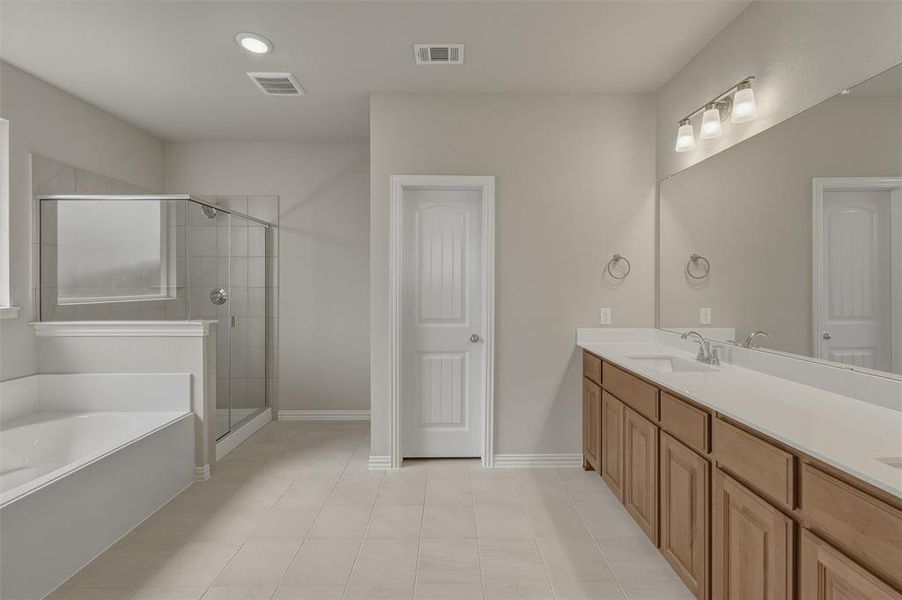 Spacious bathroom featuring a dual vanity with light-toned countertops, a glass-enclosed shower, a separate soaking tub, and neutral-toned floor tiling Spacious bathroom featuring a dual vanity with light-toned countertops, a glass-enclosed shower, a separate soaking tub, and neutral-toned floor tiling