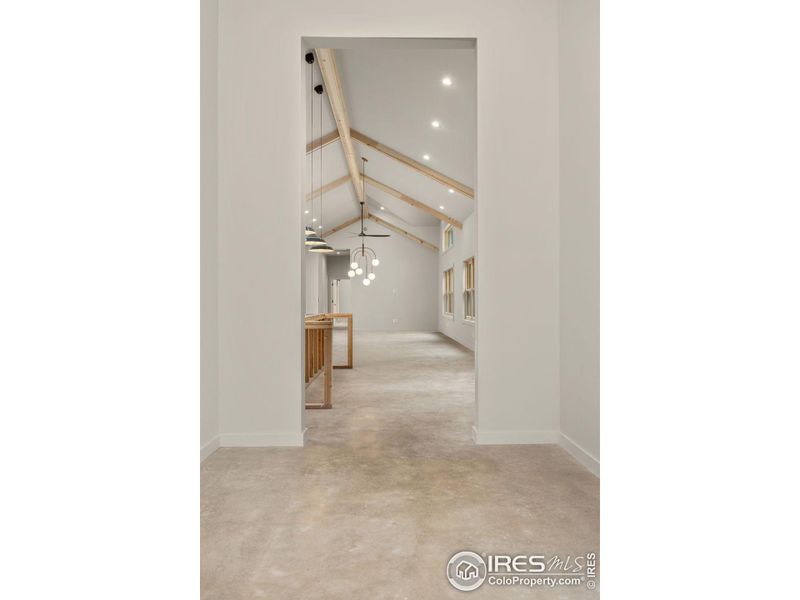 View of the main living space from the foyer with soaring vaulted ceilings and custom wood beam detailing View of the main living space from the foyer with soaring vaulted ceilings and custom wood beam detailing