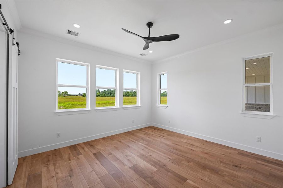 Spacious primary bedroom featuring elegant LVP floors, abundant natural light through multiple windows, and a sleek ceiling fan for comfort and style.