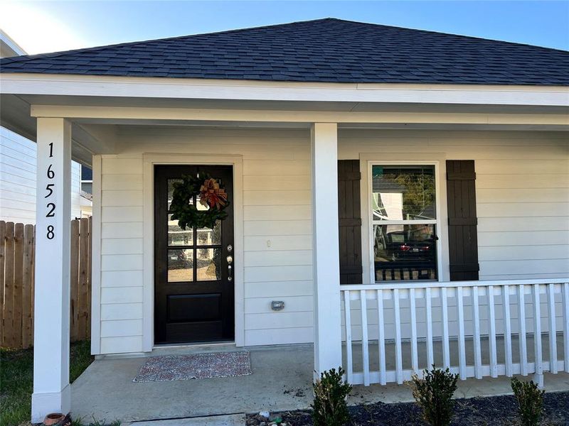 Charming single-story home featuring a welcoming covered front entrance, classic white siding with contrasting dark shutters, and a small, inviting front porch with a white railing. The house number is prominently displayed for easy identification.