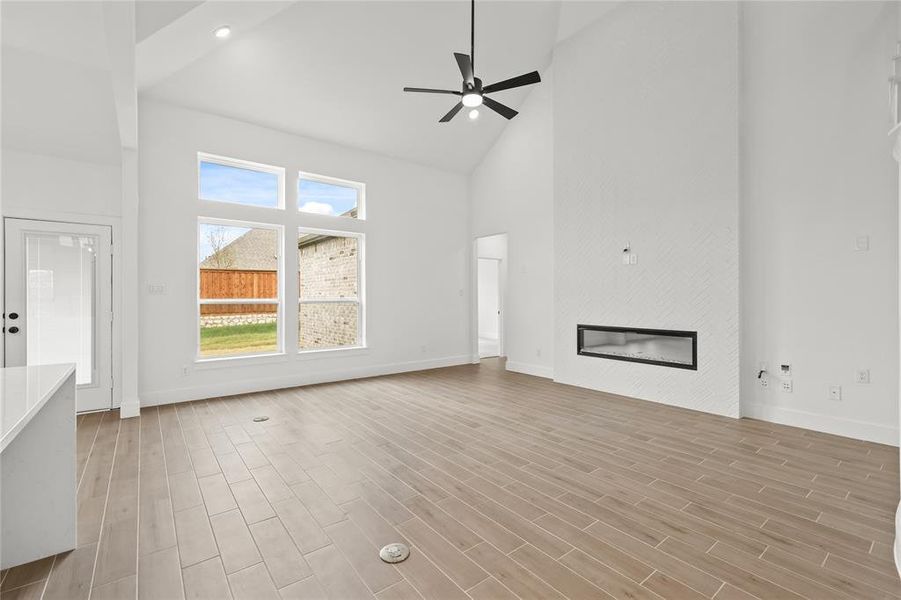 Unfurnished living room featuring light hardwood / wood-style floors, high vaulted ceiling, and ceiling fan