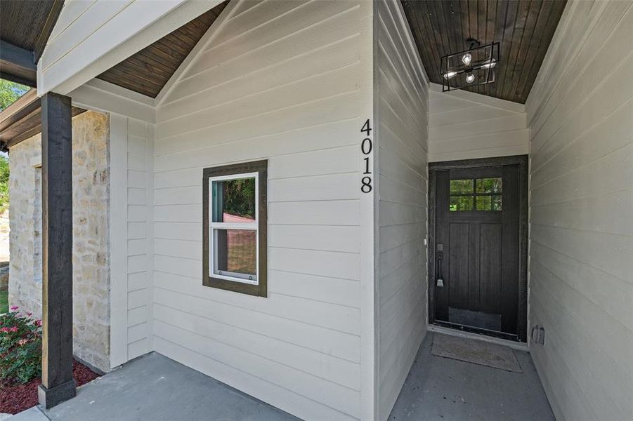 Covered front entry featuring a dark wood-finish door with glass inserts, house numbers, and a contemporary ceiling light fixture