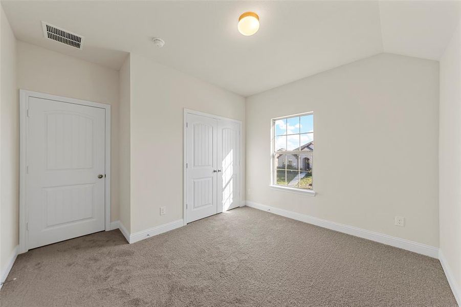 Unfurnished bedroom featuring light carpet and vaulted ceiling