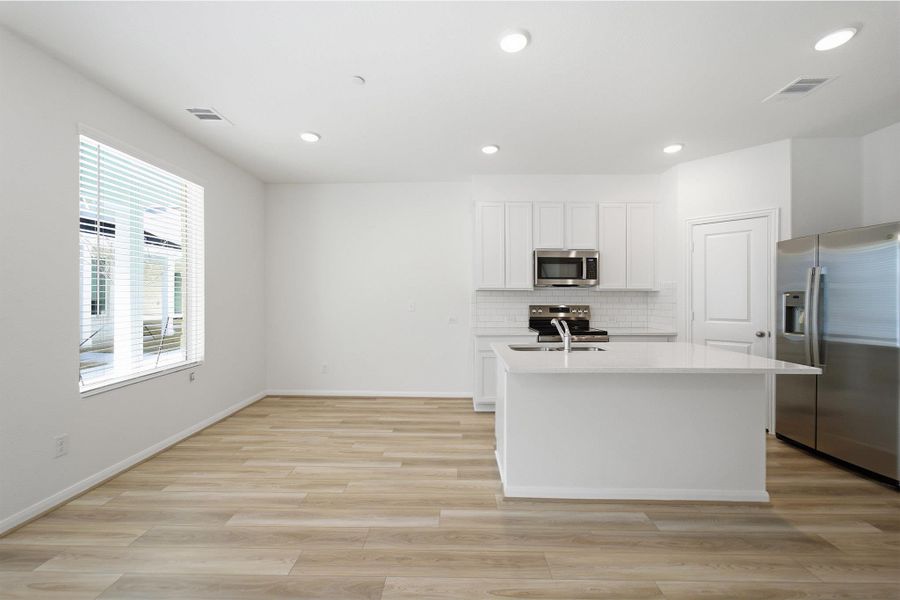 Kitchen with stainless steel appliances, an island with sink, white cabinetry, light wood-style floors, and light stone counters Kitchen with stainless steel appliances, an island with sink, white cabinetry, light wood-style floors, and light stone counters