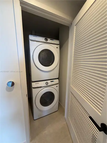 Stacked laundry center featuring high-efficiency washer and dryer, tile flooring, and louvered closet door