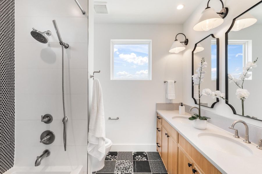 Dual vanities, warm wood cabinetry, designer lighting, playful patterned tile, and a thoughtfully appointed tub and shower create a space with both function and personality.