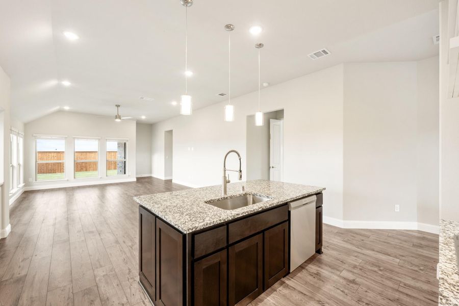 Kitchen island with granite countertop, sink, and dark cabinets, open to living area with hardwood floors and pendant lights Kitchen island with granite countertop, sink, and dark cabinets, open to living area with hardwood floors and pendant lights