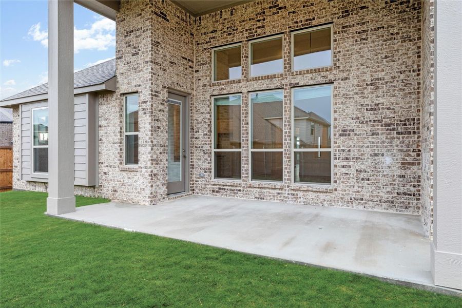 Back of brick home with covered patio, large windows, and green lawn