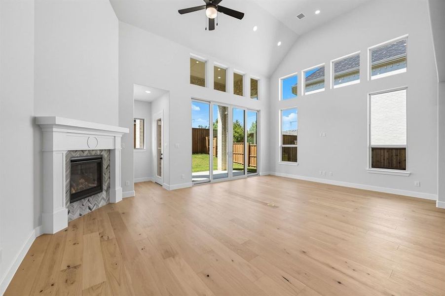 Unfurnished living room featuring a high end fireplace, high vaulted ceiling, light wood-style floors, a ceiling fan, and recessed lighting