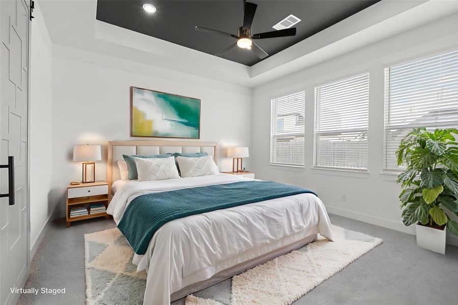 SPACIOUS PRIMARY BEDROOM WITH TRAY CEILING, MODERN FAN, AND LARGE WINDOWS FOR NATURAL LIGHT. SPACIOUS PRIMARY BEDROOM WITH TRAY CEILING, MODERN FAN, AND LARGE WINDOWS FOR NATURAL LIGHT.