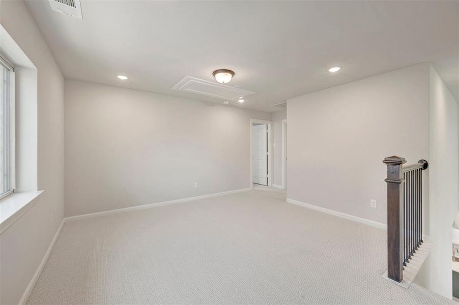 Carpeted upper-level landing featuring a wood banister, recessed lighting, and a prominent window