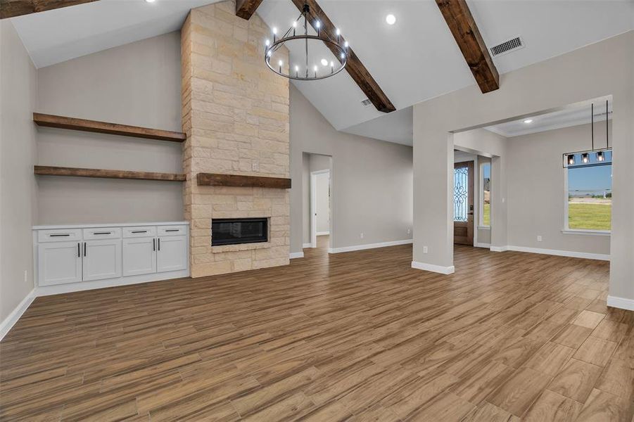 Unfurnished living room with beamed ceiling, a chandelier, wood finished floors, recessed lighting, and a stone fireplace Unfurnished living room with beamed ceiling, a chandelier, wood finished floors, recessed lighting, and a stone fireplace