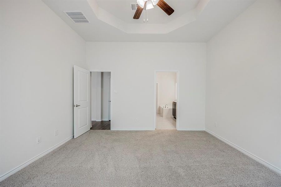 Unfurnished bedroom featuring a high ceiling, ceiling fan, light carpet, ensuite bathroom, and a tray ceiling