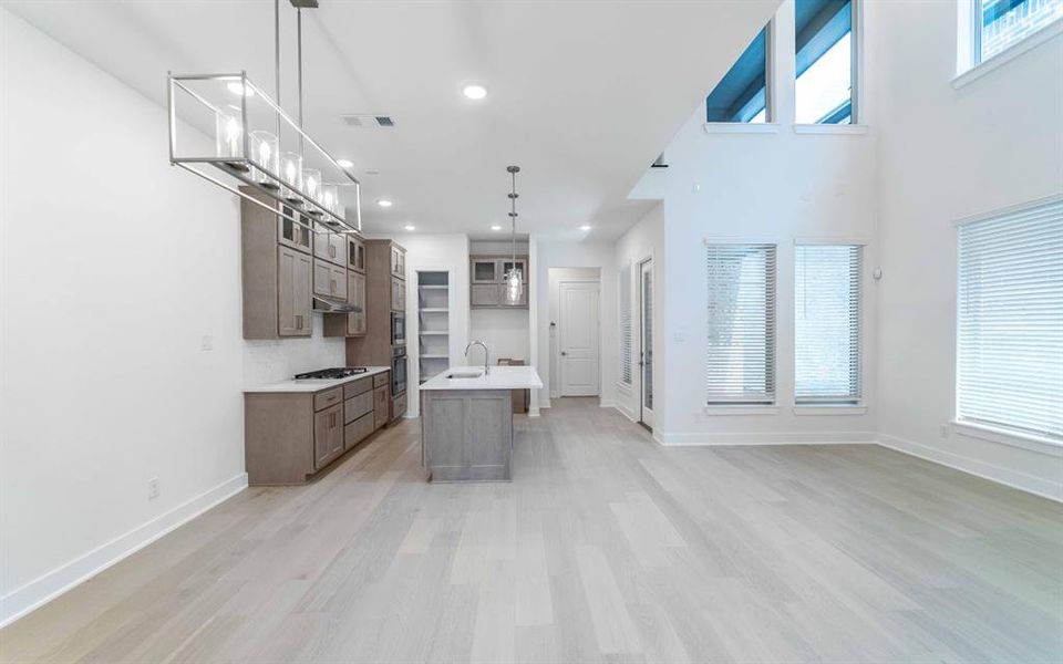 Open-concept living area featuring a kitchen with shaker-style cabinetry, a central island with a sink, and stainless steel appliances