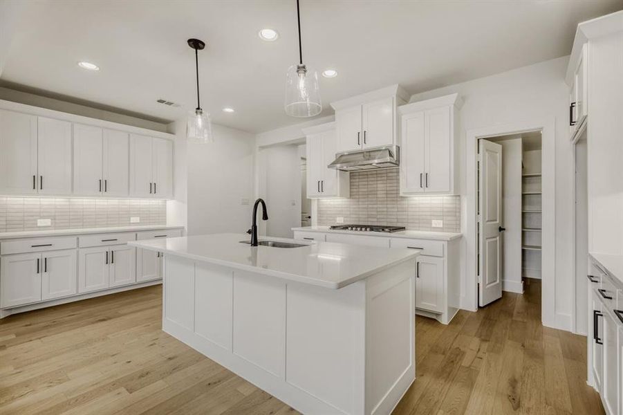 Kitchen featuring a center island with sink, light wood finished floors, hanging light fixtures, and white cabinetry