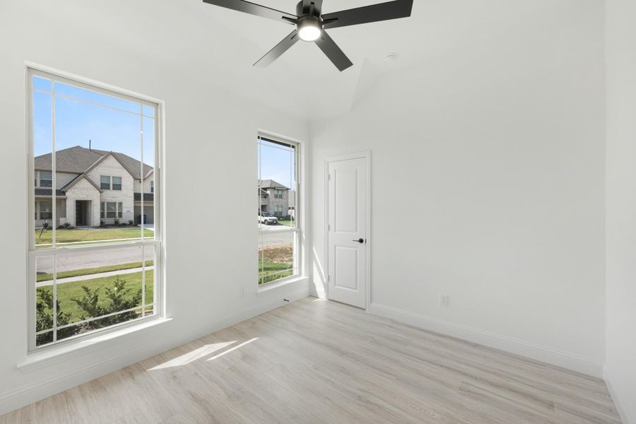 Empty bedroom with light wood floors, ceiling fan, and two large windows with neighborhood view