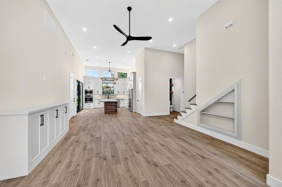 Unfurnished living room featuring built in shelves, a towering ceiling, recessed lighting, light wood-type flooring, and a ceiling fan