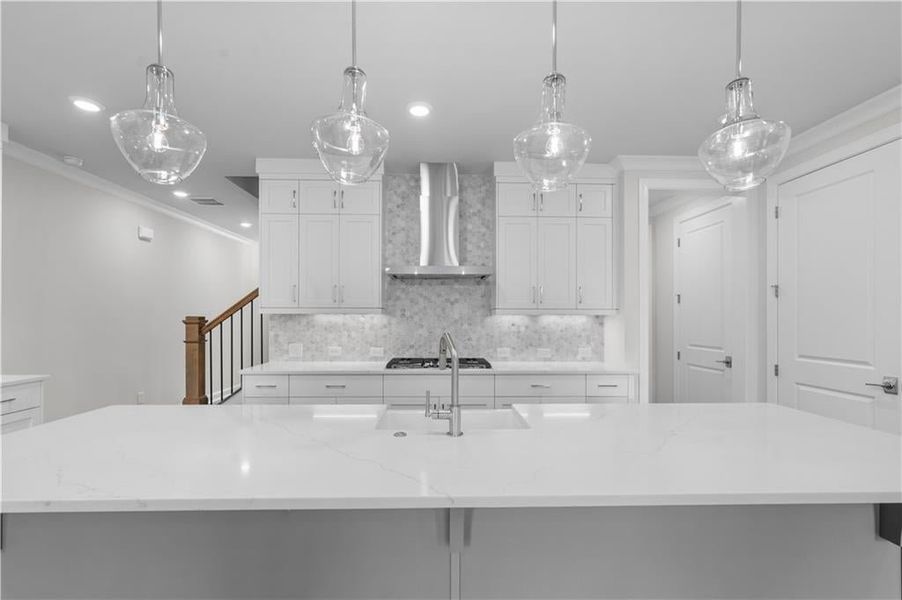 Kitchen featuring ornamental molding, backsplash, pendant lighting, white cabinets, and a center island with sink Kitchen featuring ornamental molding, backsplash, pendant lighting, white cabinets, and a center island with sink